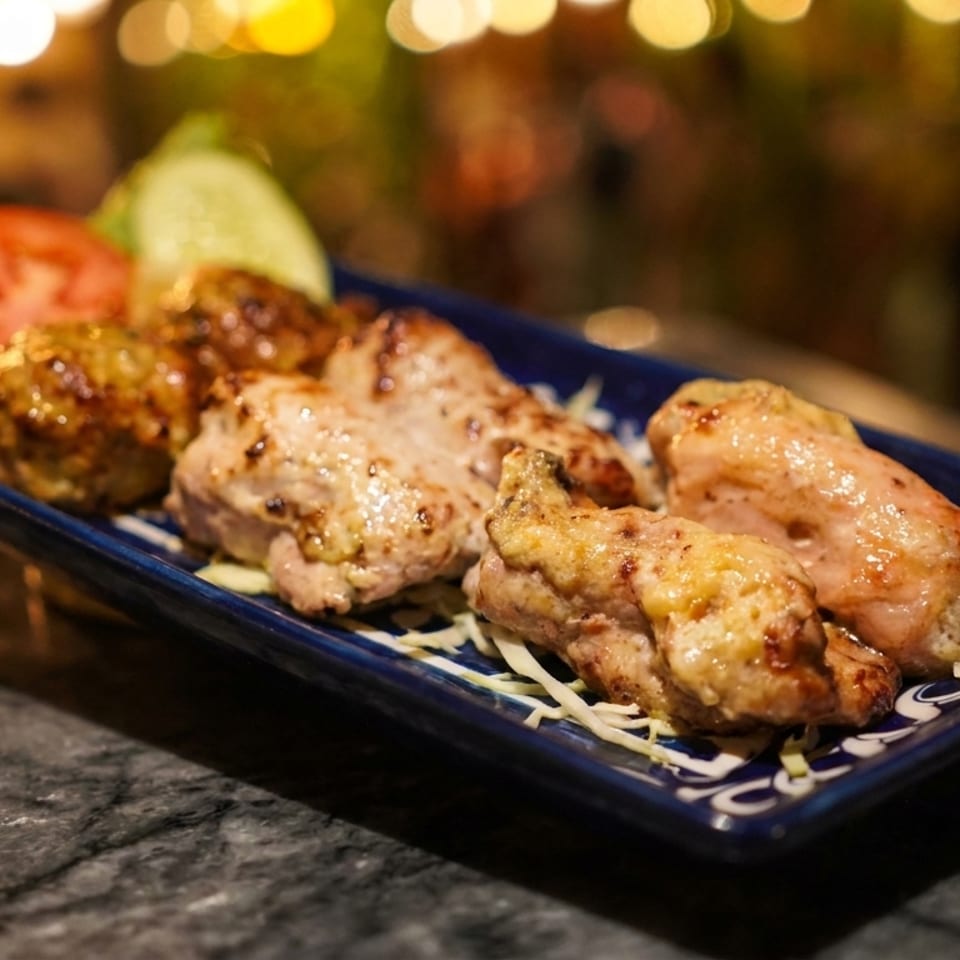 Grilled chicken pieces and meatballs with tomato and cucumber slices on a blue plate.